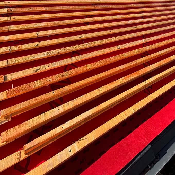 Close view of treated timber battens set to gauge over red roofing membrane