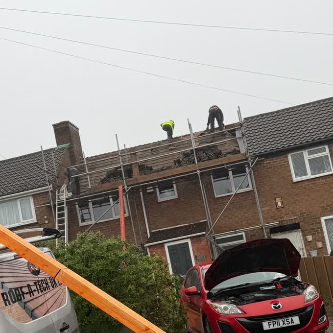 Two roofers stripping old tiles from a terraced roof from a scaffold